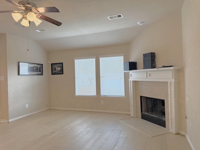 unfurnished living room with light wood-type flooring, visible vents, vaulted ceiling, and a tiled fireplace