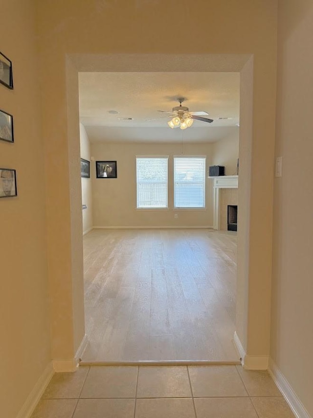 interior space with a ceiling fan, a fireplace, baseboards, and light tile patterned floors