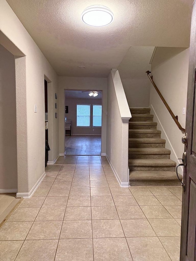 hall with stairs, a textured ceiling, baseboards, and light tile patterned floors