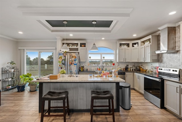 kitchen with wall chimney range hood, appliances with stainless steel finishes, pendant lighting, and a tray ceiling