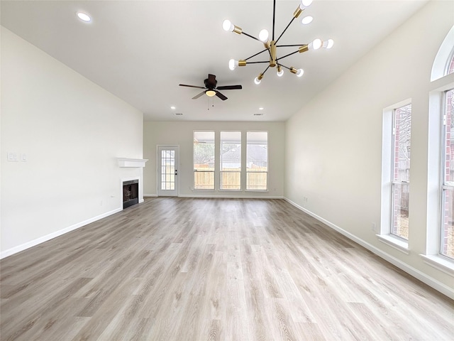 unfurnished living room featuring ceiling fan with notable chandelier and light hardwood / wood-style floors