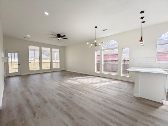 unfurnished living room featuring ceiling fan with notable chandelier and light wood-type flooring