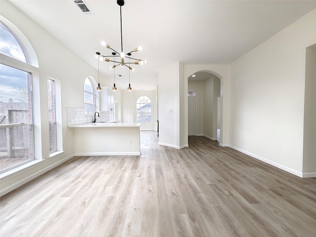 unfurnished living room with sink, a chandelier, and light hardwood / wood-style floors