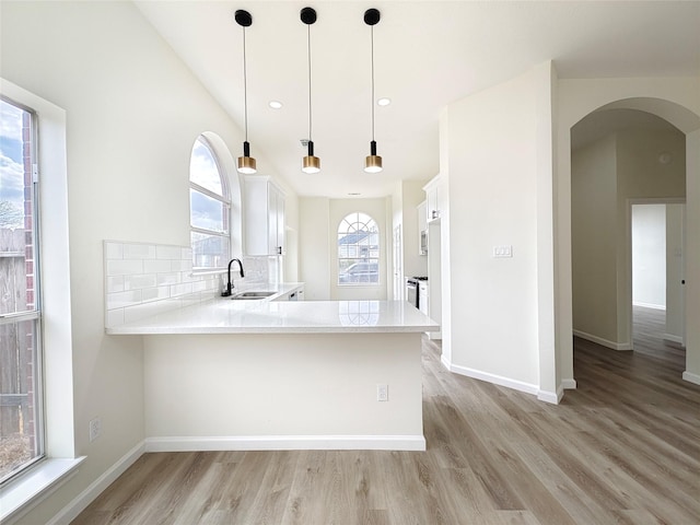 kitchen with sink, backsplash, white cabinets, decorative light fixtures, and kitchen peninsula