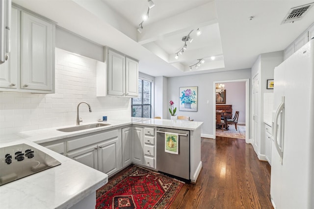 kitchen featuring dishwasher, sink, white fridge with ice dispenser, kitchen peninsula, and a raised ceiling