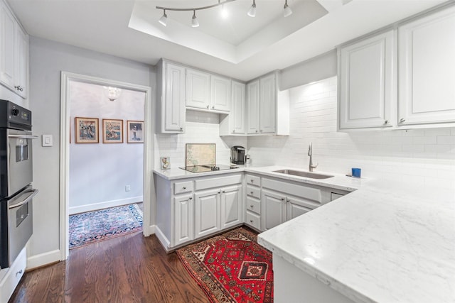 kitchen with sink, black electric stovetop, a tray ceiling, white cabinets, and stainless steel double oven