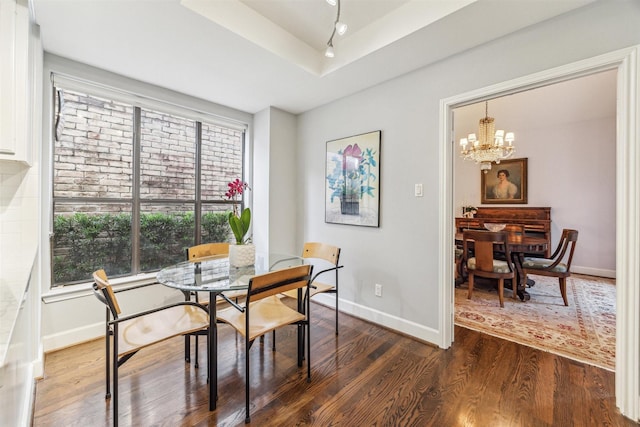 dining area with dark wood-type flooring, a tray ceiling, and a notable chandelier