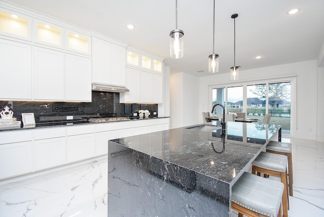 kitchen with an island with sink, white cabinetry, sink, a kitchen breakfast bar, and hanging light fixtures