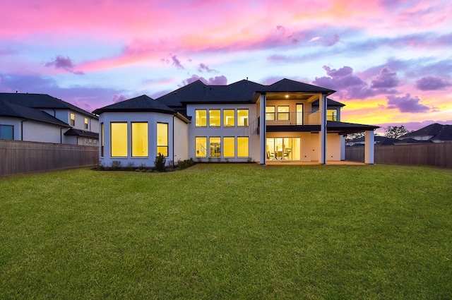 back house at dusk featuring a patio, a balcony, and a yard