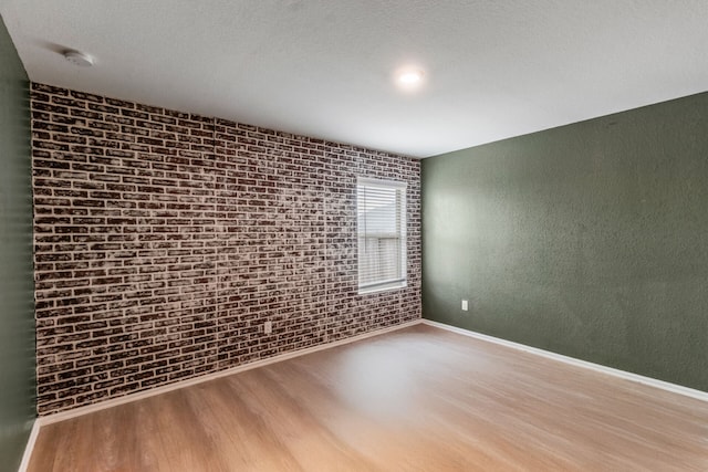 unfurnished room with wood-type flooring and brick wall