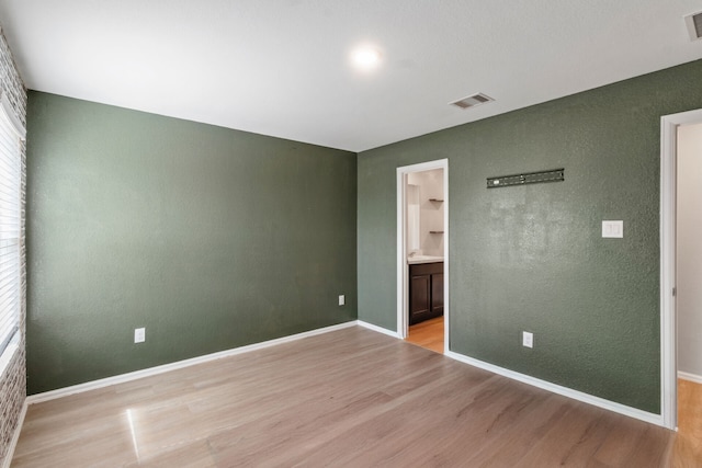 unfurnished bedroom featuring ensuite bathroom and light hardwood / wood-style flooring