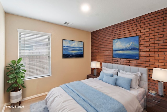 bedroom with brick wall and light hardwood / wood-style floors