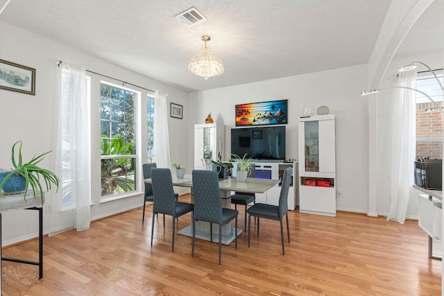 dining space with a chandelier, a textured ceiling, and light wood-type flooring