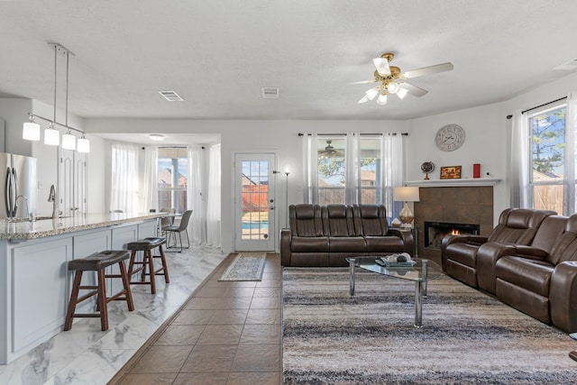 living room featuring ceiling fan, a fireplace, and a textured ceiling