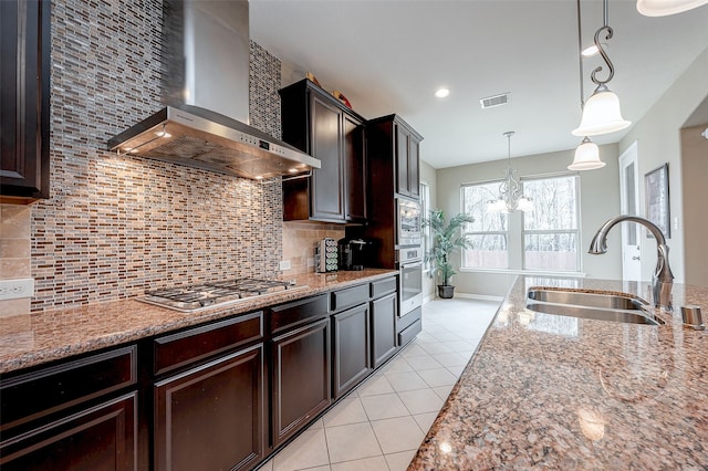 kitchen with wall chimney range hood, sink, appliances with stainless steel finishes, hanging light fixtures, and light stone countertops