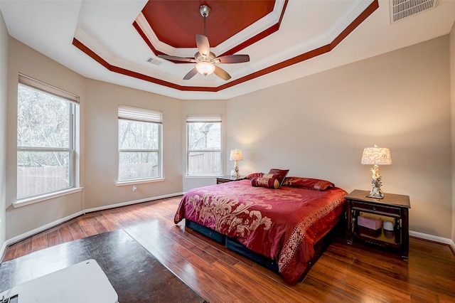 bedroom with dark hardwood / wood-style floors, ceiling fan, ornamental molding, and a tray ceiling