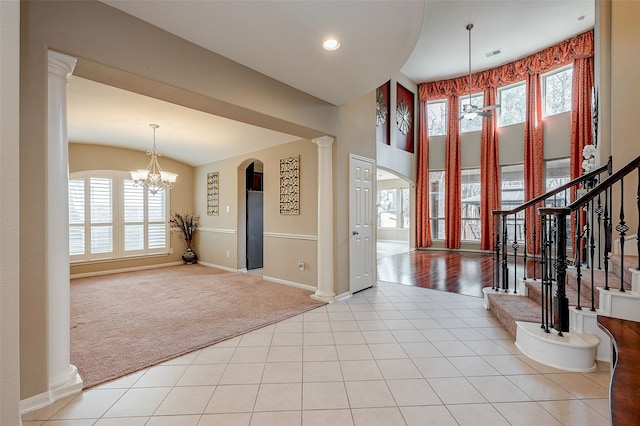 carpeted entryway featuring an inviting chandelier, a towering ceiling, and decorative columns