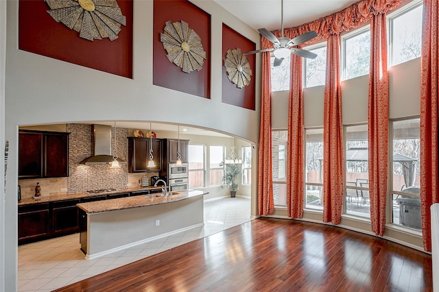 kitchen featuring a kitchen island with sink, light wood-type flooring, wall chimney exhaust hood, and appliances with stainless steel finishes