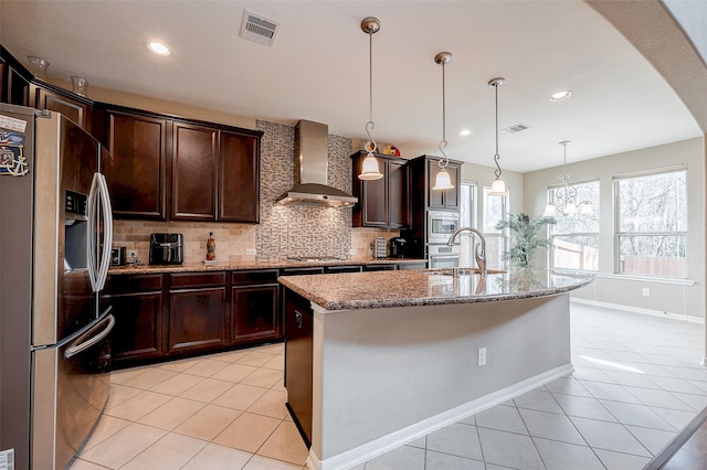 kitchen with light tile patterned flooring, wall chimney exhaust hood, sink, stainless steel appliances, and a kitchen island with sink