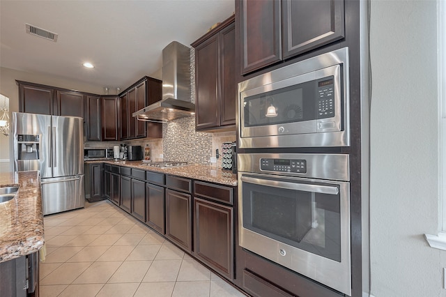 kitchen with tasteful backsplash, stainless steel appliances, light stone countertops, and wall chimney range hood