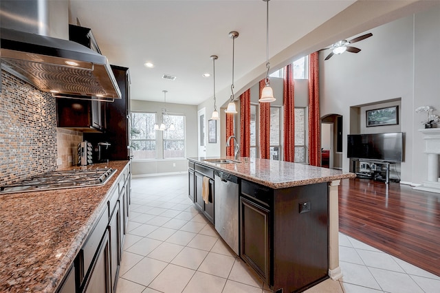 kitchen featuring appliances with stainless steel finishes, pendant lighting, ventilation hood, sink, and a center island with sink