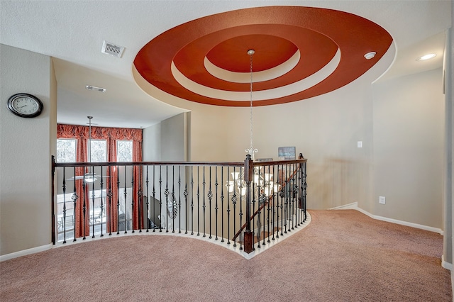 hallway featuring a tray ceiling, carpet floors, and a chandelier