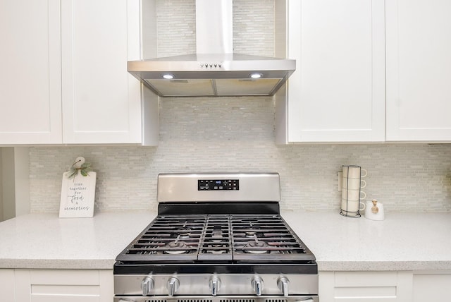 kitchen featuring gas stove, white cabinetry, tasteful backsplash, light stone countertops, and wall chimney range hood