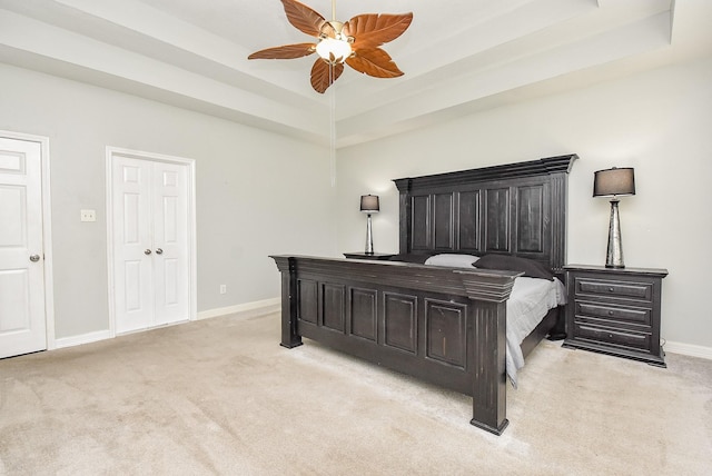 bedroom featuring light carpet, ceiling fan, and a tray ceiling