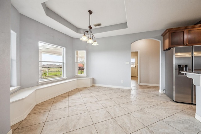 unfurnished dining area with a chandelier, a raised ceiling, and light tile patterned floors