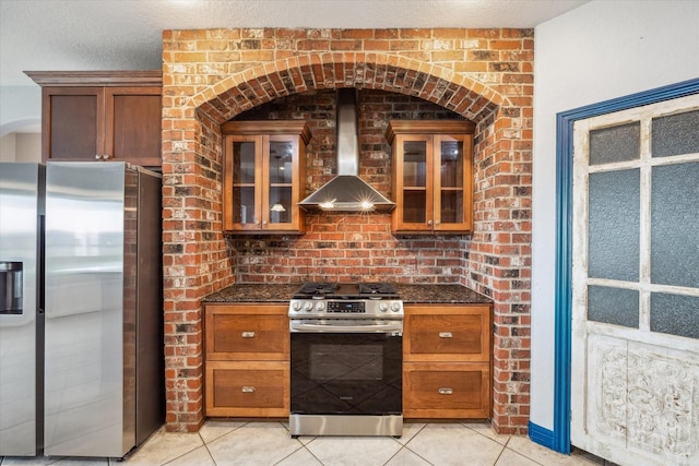 kitchen featuring light tile patterned floors, appliances with stainless steel finishes, a textured ceiling, dark stone counters, and wall chimney exhaust hood