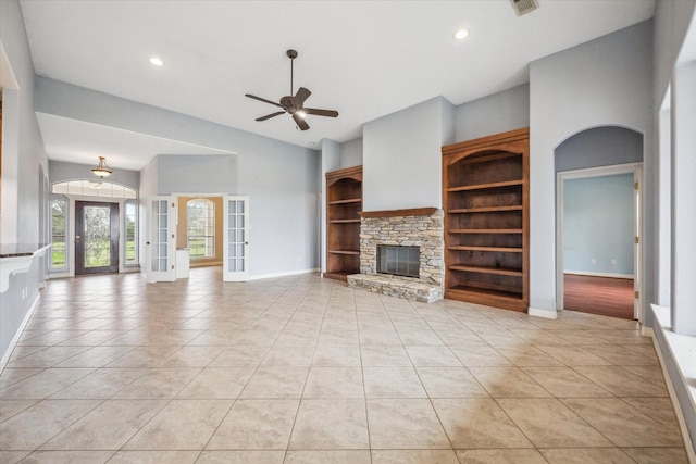 unfurnished living room with light tile patterned floors, a stone fireplace, french doors, and ceiling fan