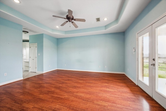 spare room with a tray ceiling, light hardwood / wood-style flooring, french doors, and ceiling fan