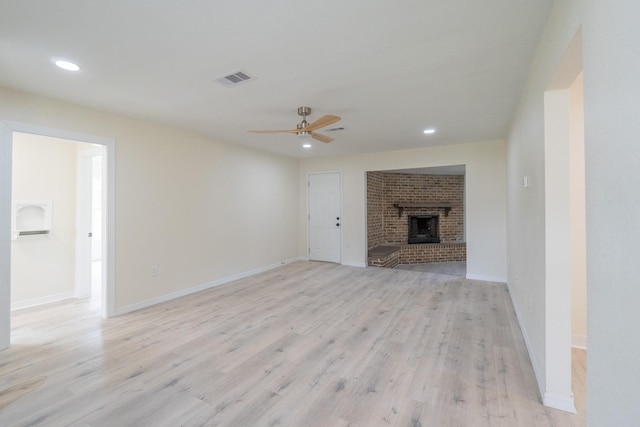 unfurnished living room with ceiling fan, a brick fireplace, and light wood-type flooring