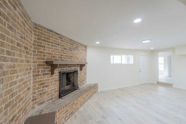 unfurnished living room with brick wall, light wood-type flooring, and a fireplace