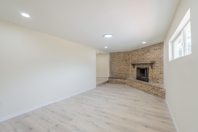 unfurnished living room featuring a brick fireplace and light wood-type flooring