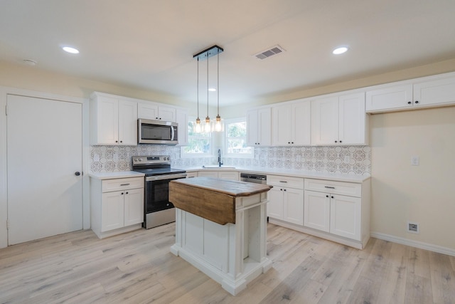 kitchen with sink, hanging light fixtures, stainless steel appliances, a center island, and white cabinets