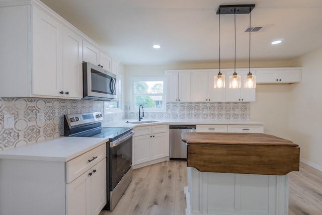 kitchen with sink, appliances with stainless steel finishes, hanging light fixtures, white cabinets, and a kitchen island