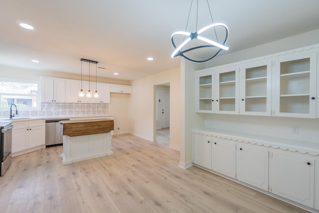 kitchen featuring a kitchen island, white cabinets, hanging light fixtures, stainless steel appliances, and light hardwood / wood-style flooring