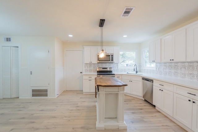 kitchen featuring a kitchen island, decorative light fixtures, white cabinetry, light hardwood / wood-style floors, and stainless steel appliances