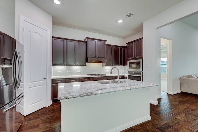 kitchen featuring dark hardwood / wood-style floors, sink, light stone counters, stainless steel appliances, and a center island with sink