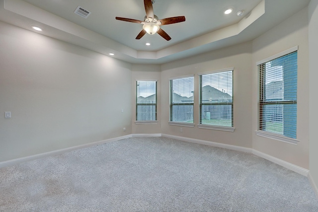 carpeted spare room with a raised ceiling and ceiling fan