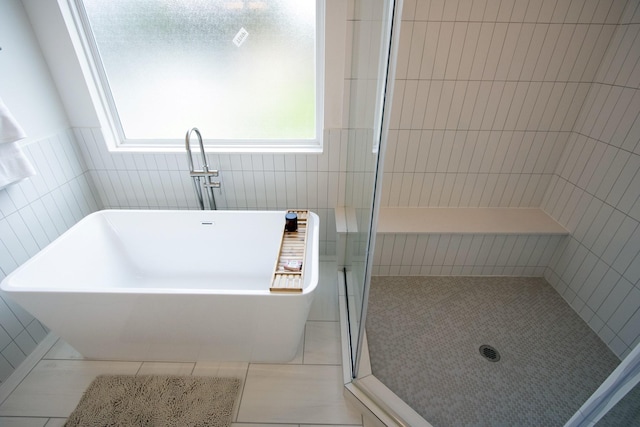 bathroom featuring shower with separate bathtub, tile walls, and tile patterned floors