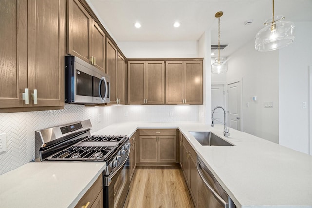 kitchen featuring pendant lighting, sink, backsplash, stainless steel appliances, and light hardwood / wood-style floors