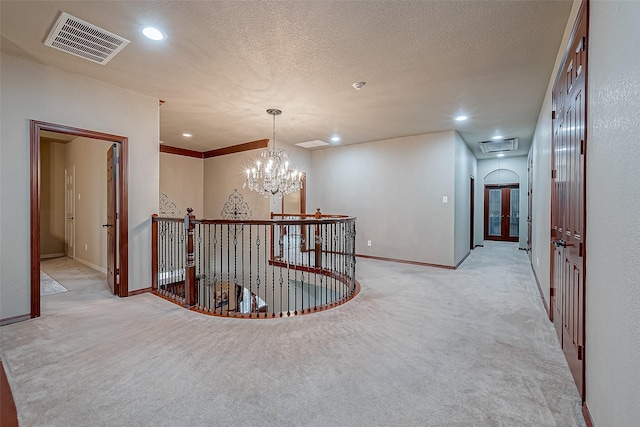 hall featuring an inviting chandelier, light carpet, and a textured ceiling