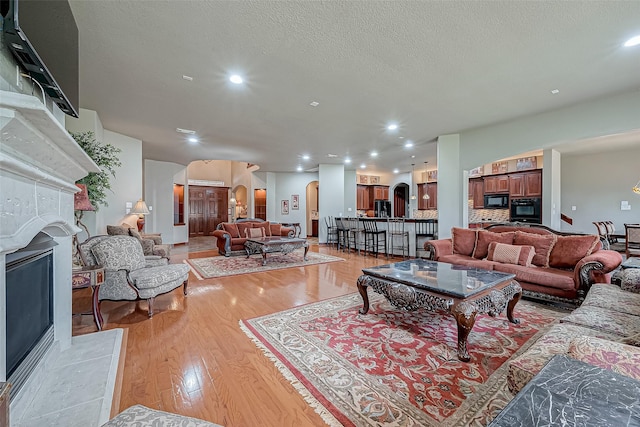 living room with a tiled fireplace, light hardwood / wood-style flooring, and a textured ceiling