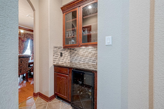 bar featuring wine cooler, dark stone counters, decorative backsplash, and light tile patterned floors