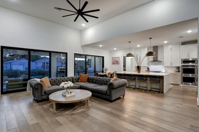 living room featuring a towering ceiling, light hardwood / wood-style flooring, and ceiling fan