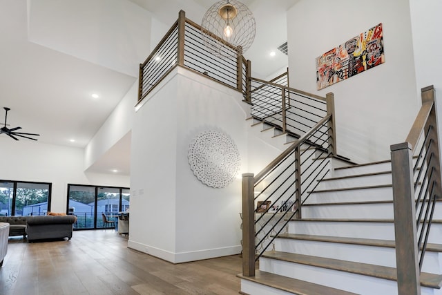 staircase with ceiling fan, a towering ceiling, and hardwood / wood-style floors