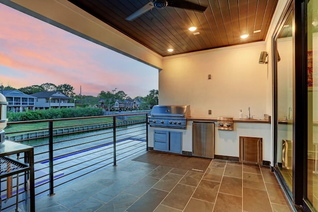 patio terrace at dusk featuring sink, ceiling fan, a grill, a balcony, and an outdoor kitchen