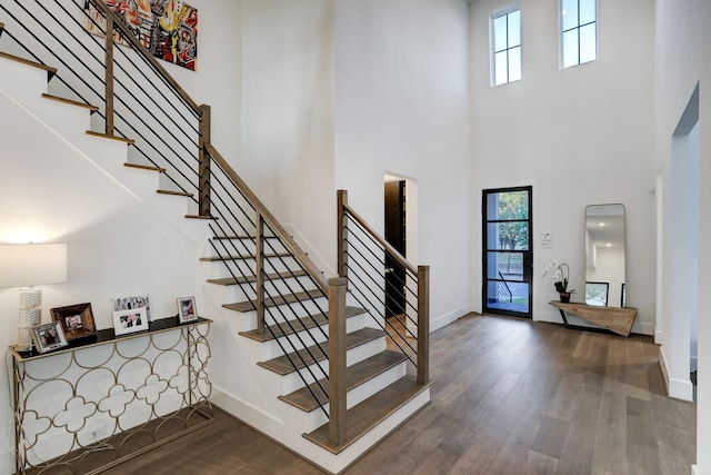 stairway with hardwood / wood-style flooring, a healthy amount of sunlight, and a high ceiling